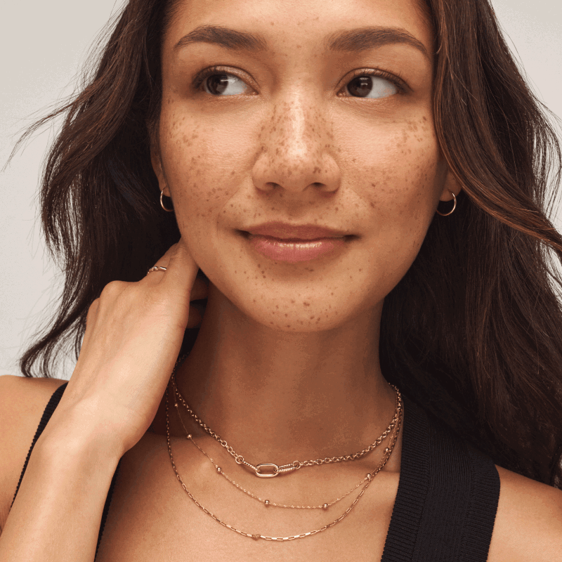 Woman wearing layered yellow gold necklaces, hoop earrings and ring. 