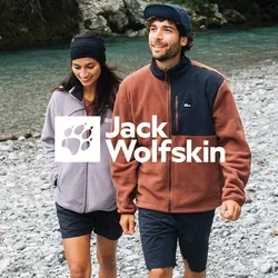 Paar, das an einem felsigen Flussufer spaziert. Frau in einer helllila Fleecejacke, Mann in einem braunen Fleece mit schwarzem Einsatz. Beide in Shorts und Sneakers.
