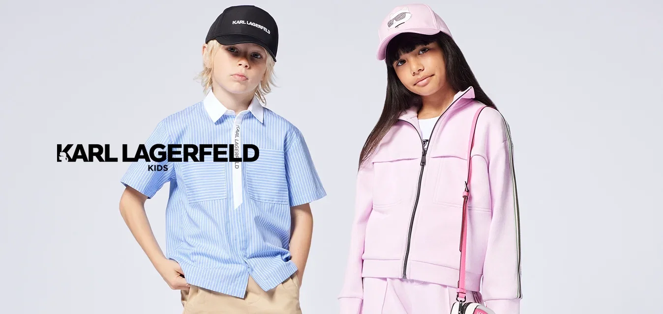 Deux enfants se tiennent debout ; l'un porte une chemise rayée bleue avec un short beige et une casquette noire, l'autre porte un survêtement rose et un chapeau avec une petite pochette.