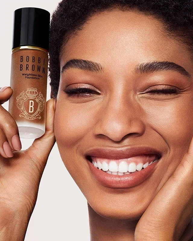 Smiling woman holding a bottle of Weightless Skin Foundation SPF 15.