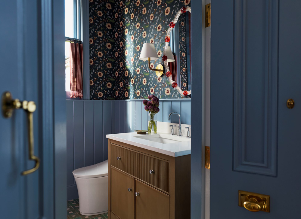 Dabito’s eclectic guest bathroom with blue paneled walls, floral wallpaper, patterned tile floor, and KOHLER vanity, faucet, and smart toilet viewed through an open door.