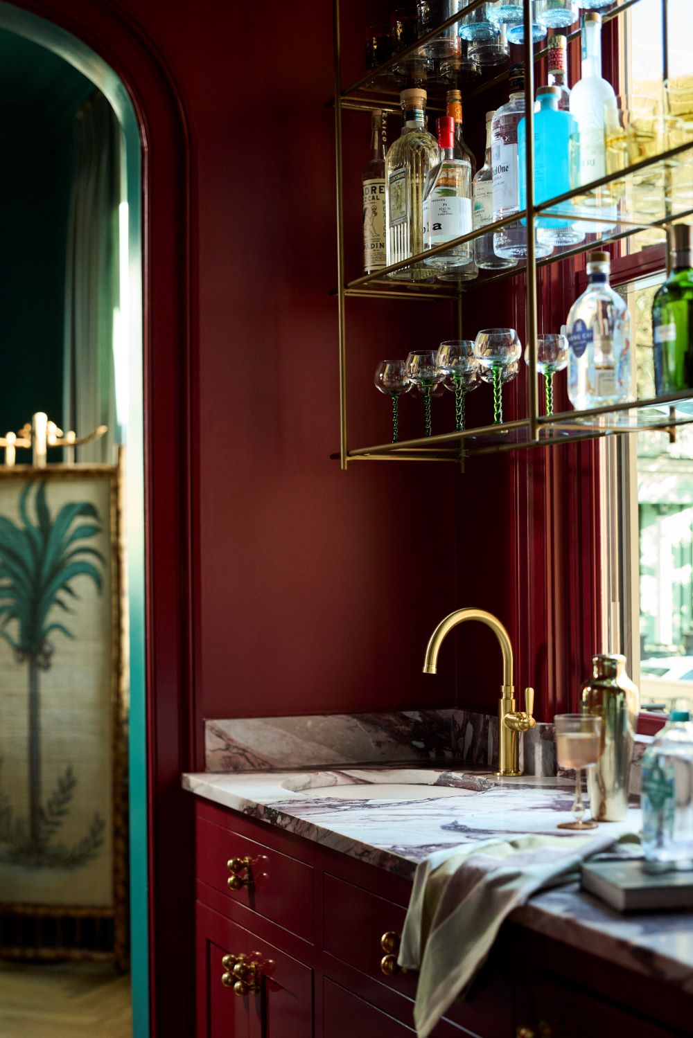 Dabito’s bold burgundy wet bar featuring a Porto Fino bar sink and Vibrant Brushed Moderne Brass faucet, styled with glassware and bottles.