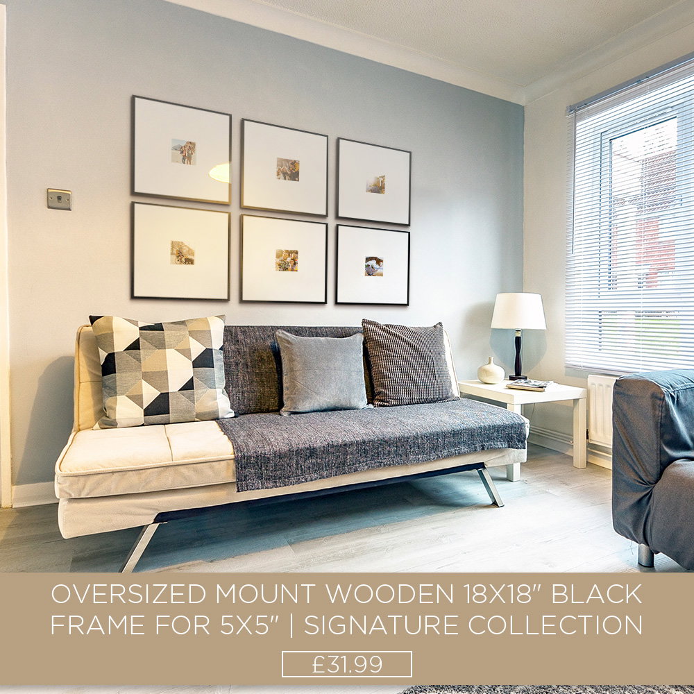 Six black oversized mount photo frames arranged in a gallery wall above a grey sofa in a modern living room.