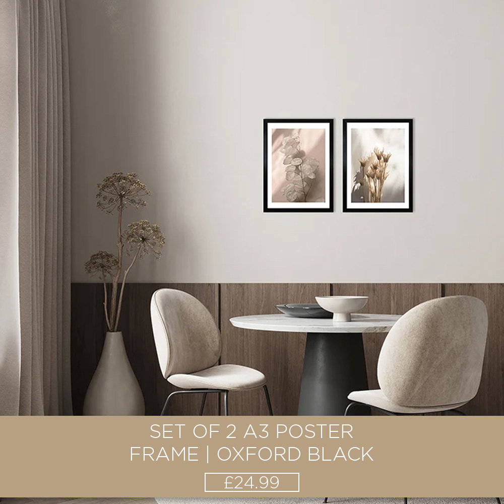 Two black A3 poster frames with botanical prints displayed above a dining table in a modern dining room.