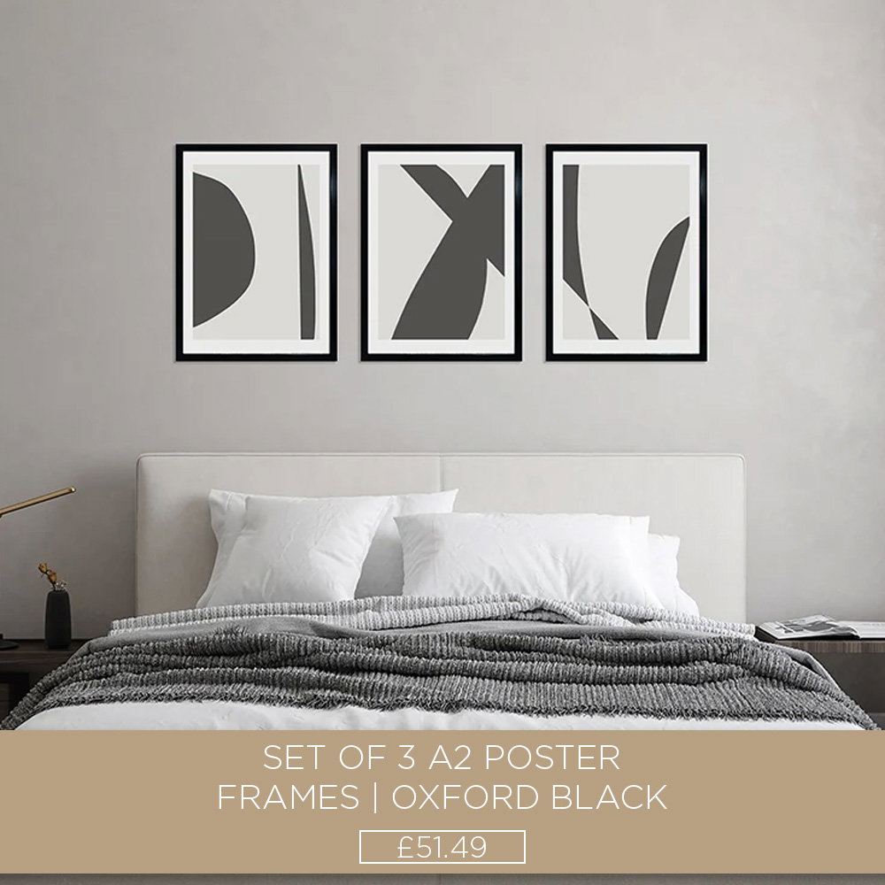 Three black A2 poster frames with abstract artwork arranged above a bed in a contemporary bedroom.