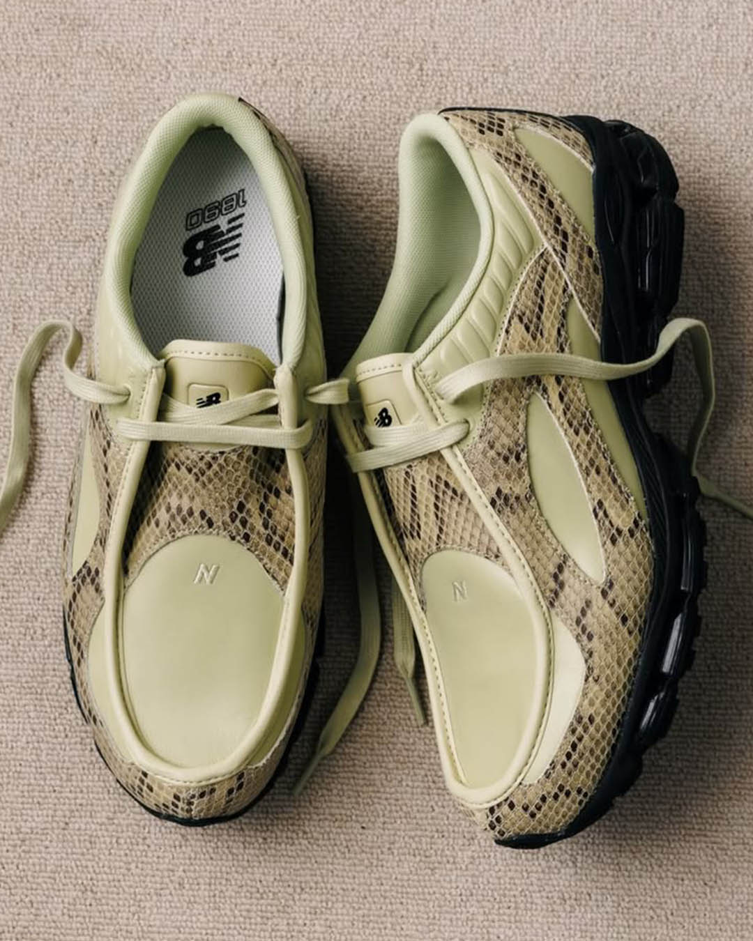 Top-down view of pale green New Balance trainers with snakeskin print panels, black soles and laces on beige carpet