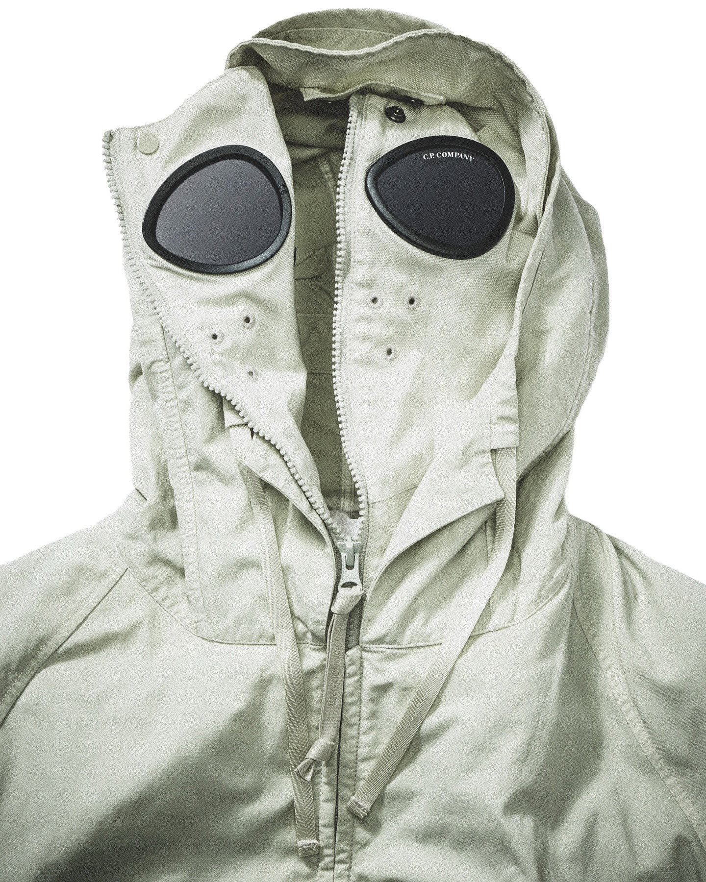 Light khaki hooded jacket with zip front and integrated round goggle lenses on the hood, C.P. Company detail