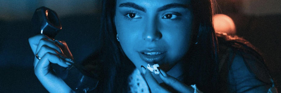 Woman watching a film holding a phone in one hand and popcorn towards mouth in the other.