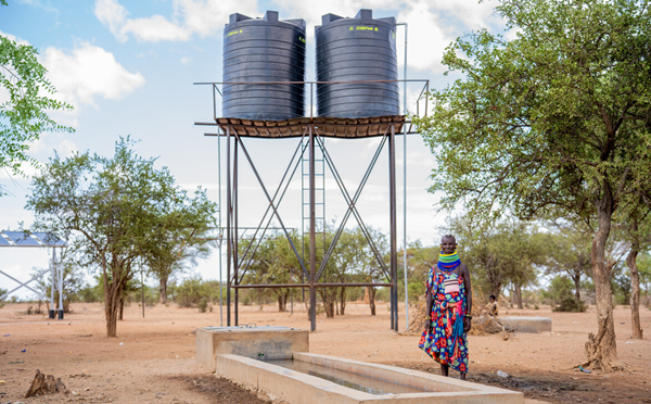 A woman stands in front of two large water tanks. Solar panels can also be seen in the background. 