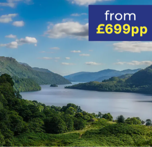 Scenic view of a tranquil lake surrounded by lush green hills under a blue sky with clouds.