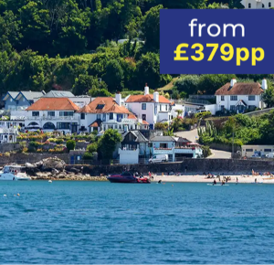 Coastal view of a seaside village with white houses and a sandy beach, boats in the water.
