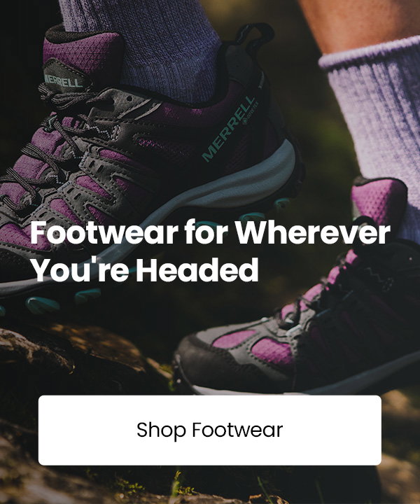 Close-up of purple and black Merrell hiking shoes worn on a rocky forest trail, with the text “Footwear for Wherever You're Headed” and a “Shop Footwear” button displayed over the image.