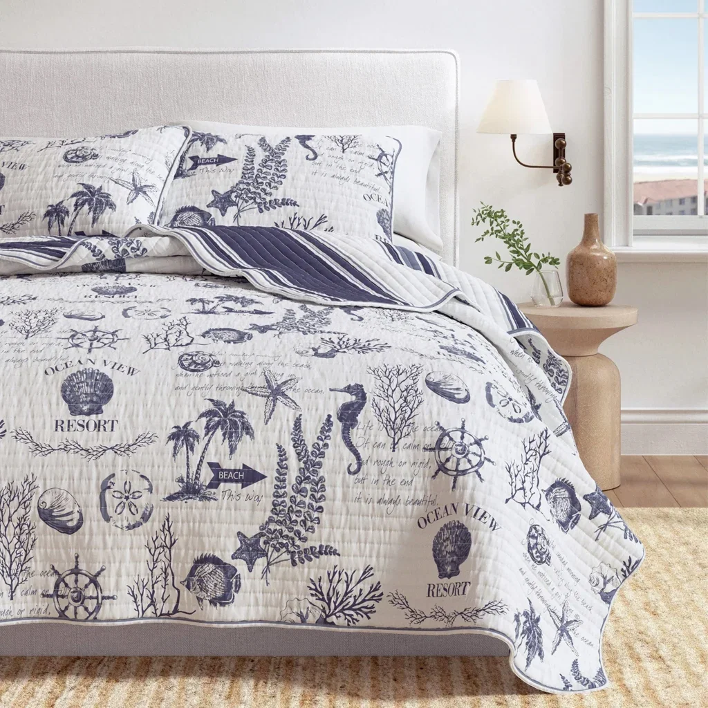 Coastal-themed bedding with navy ocean motifs, striped quilt, and white pillows on a light gray upholstered bed