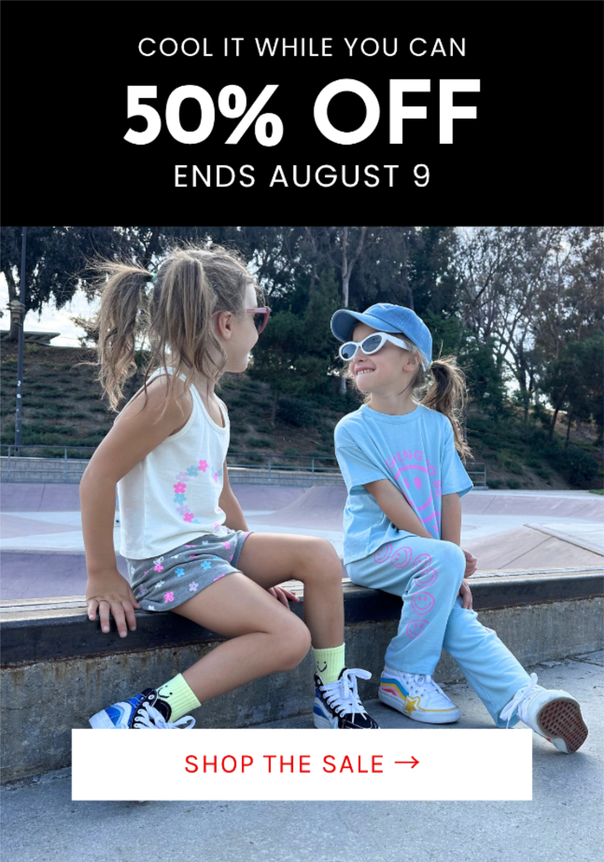 Two girls in colorful Chaser Kids outfits and sunglasses smile at each other at a skatepark for the final weekend of the 50% off sale