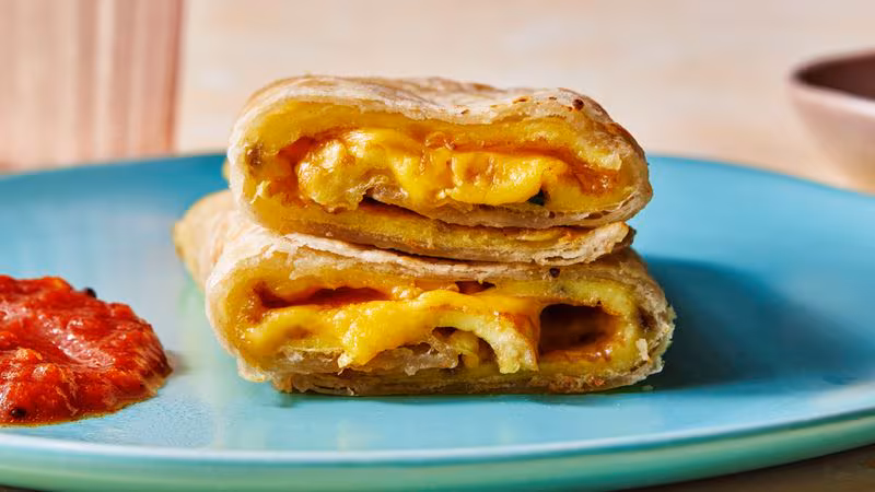 Straight-on shot of a roti omelet roll-up with sambal oelek on the side, and american cheeze oozing out