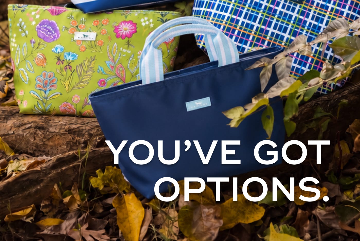 YOU'VE GOT OPTIONS. Three SCOUT bags in floral, solid blue, and plaid patterns resting on a bed of autumn leaves.