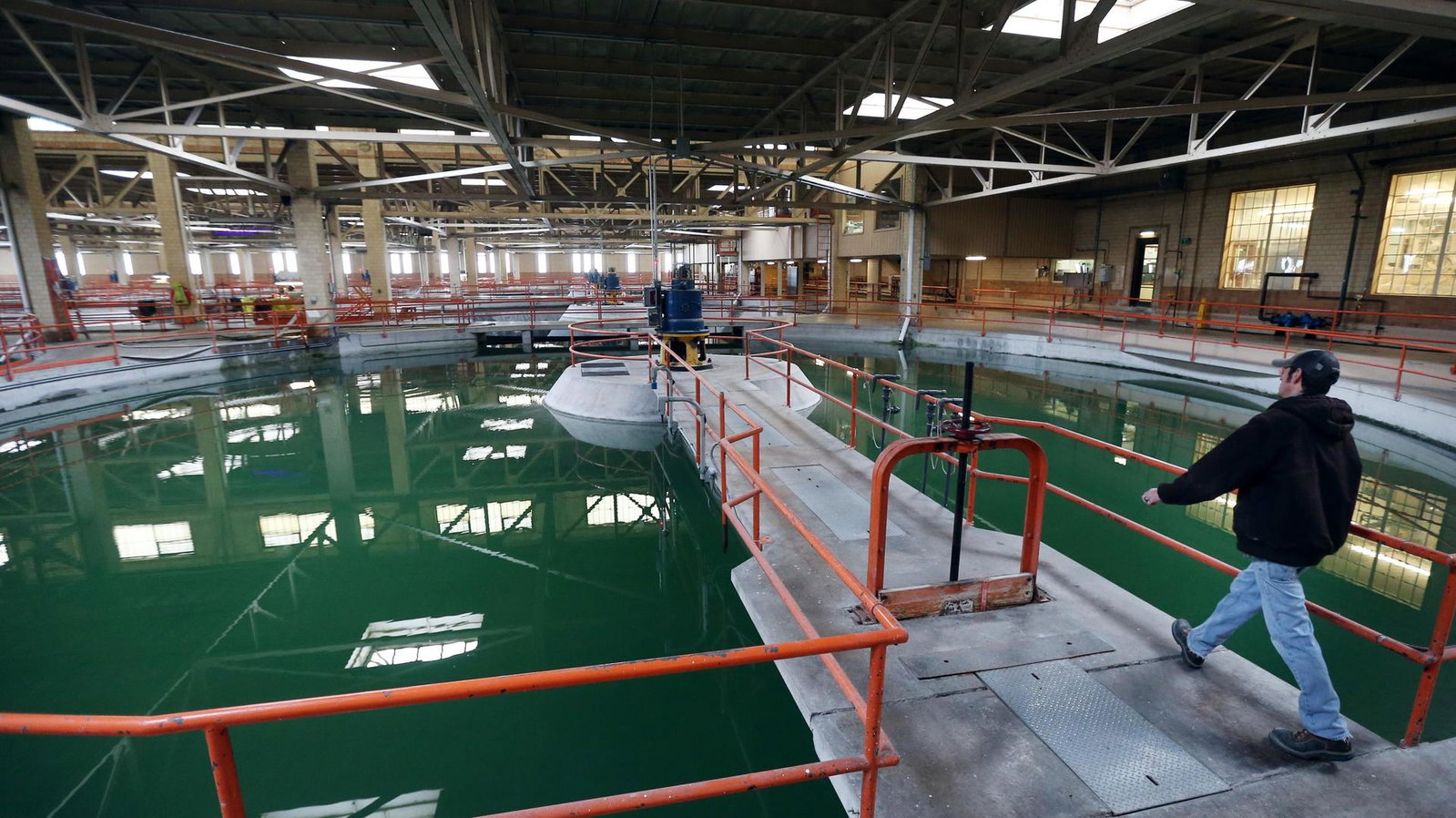 Workers on walkways over a green lagoon inside a water treatment plant.