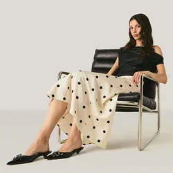 Vrouw in zwart topje en polkadotrok zittend op een zwarte moderne stoel tegen een effen lichte achtergrond.