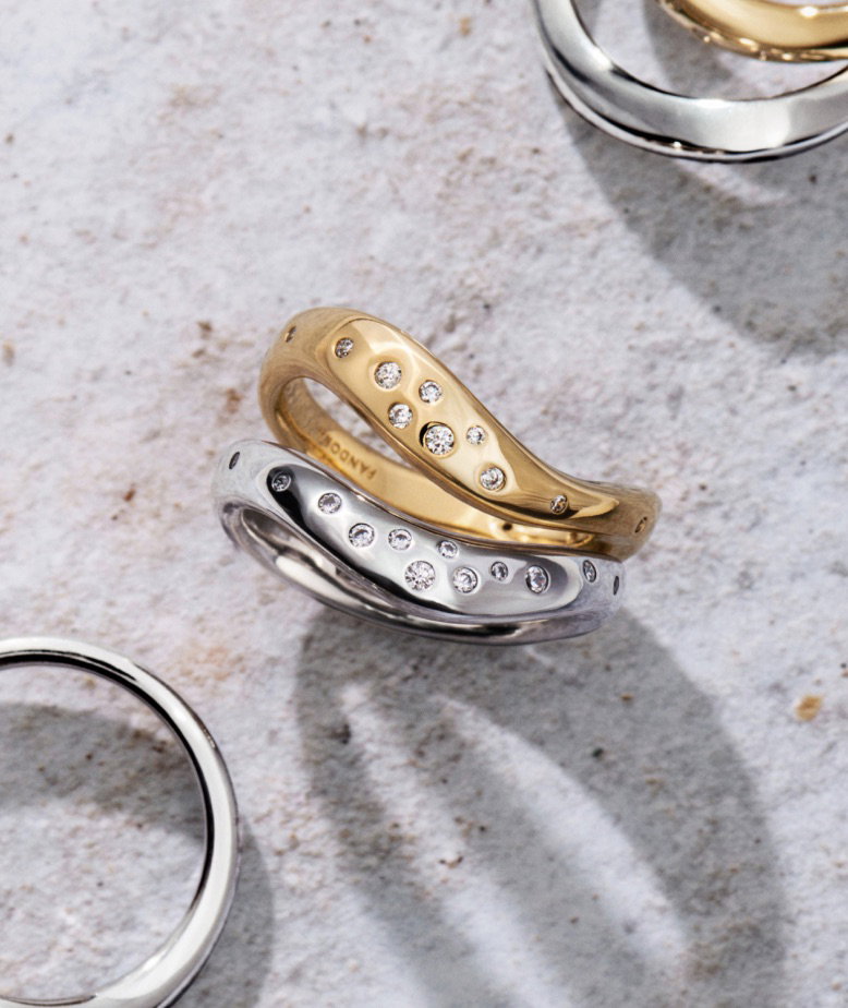 A stack of sterling silver and 14k gold-plated rings on a stone background.