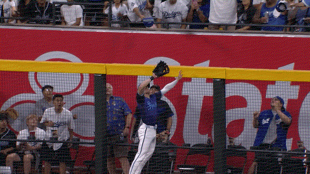An animated gif of Corbin Carroll reaching high over the wall to rob a home run
