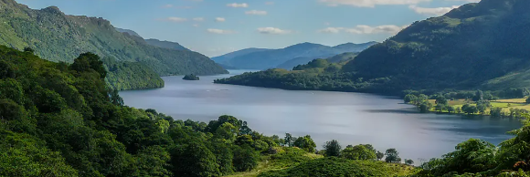 A scenic view of a tranquil lake surrounded by lush green hills under a blue sky with fluffy clouds.