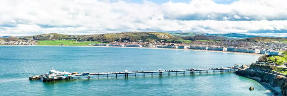 A scenic view of a coastline with a pier extending into the blue water, surrounded by hills.