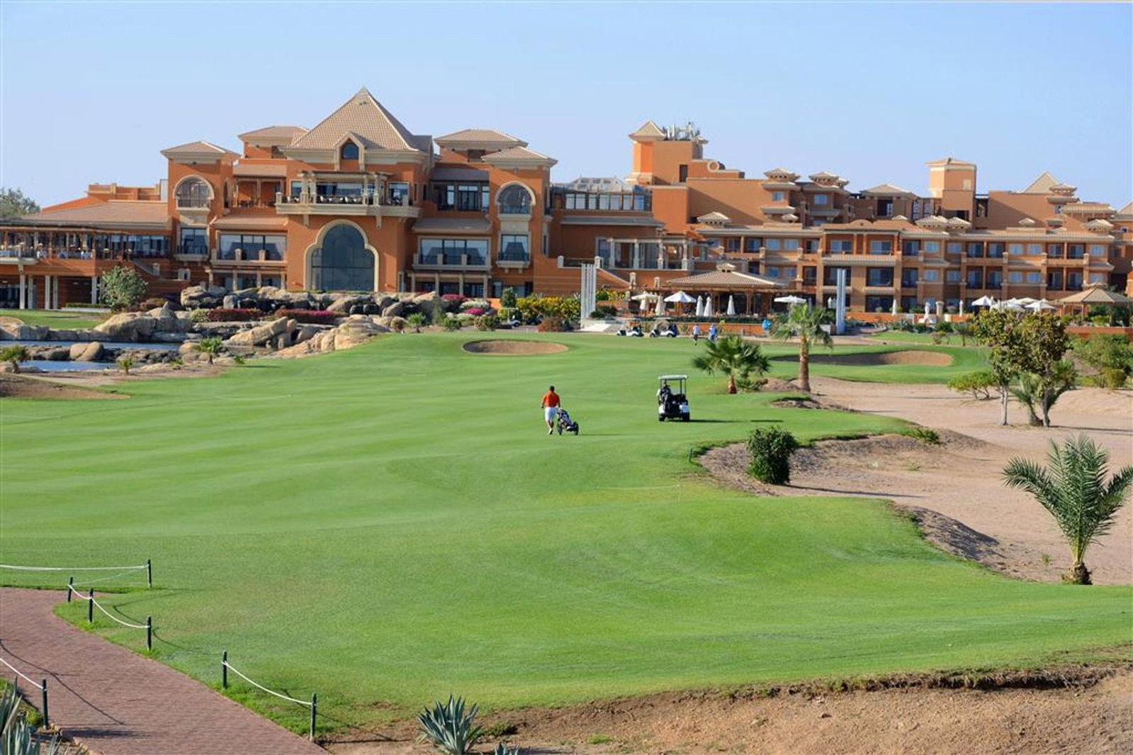 Luxury Mediterranean-style clubhouse and resort overlooking a manicured golf course with a golfer and golf buggy