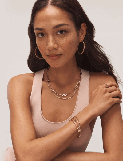 Woman wearing layered yellow gold necklaces, hoop earrings, bracelets and rings.