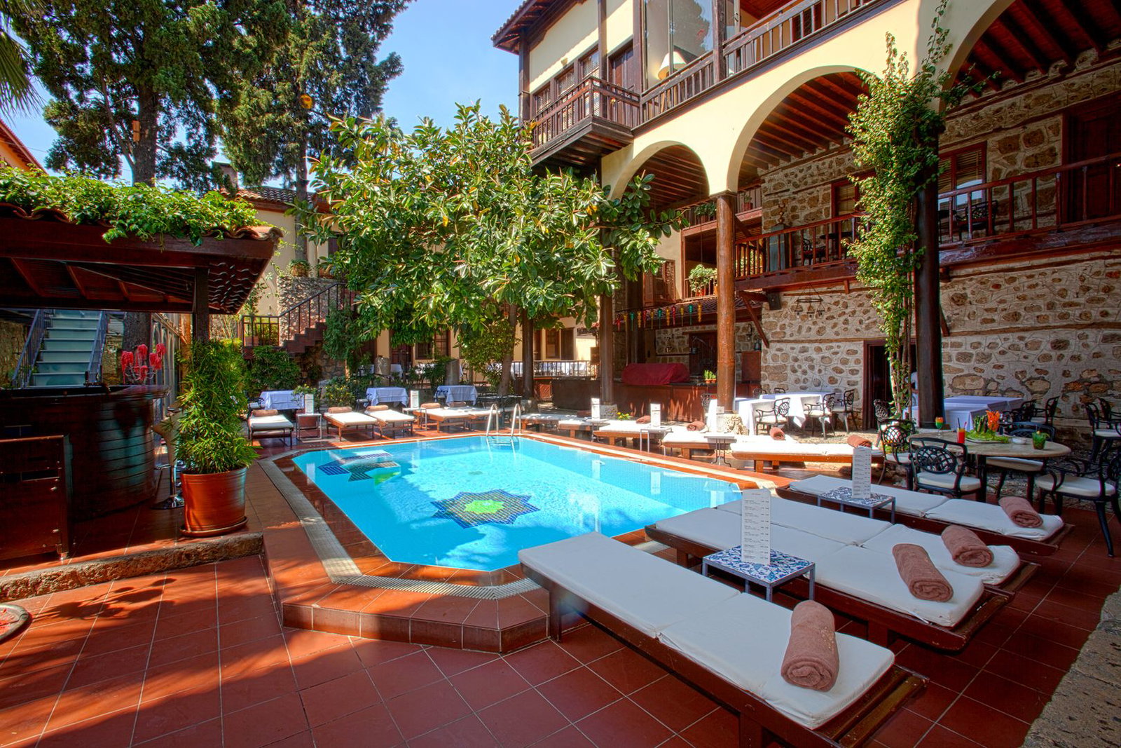 Sunny courtyard swimming pool at a boutique hotel with stone walls, wooden balconies, sun loungers and potted plants