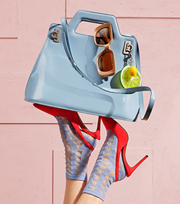 Blue bag with sunglasses and a bag charm balanced on feet wearing red high heels and blue socks.