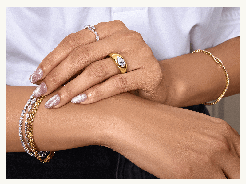 Gold dome ring with pear diamond, paired with stacked gold & diamond bracelets on model.