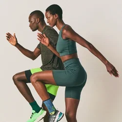 Twee atleten in sportkleding voeren hoge knieoefeningen uit tegen een vlakke achtergrond, wat de nadruk legt op fitness en coördinatie.