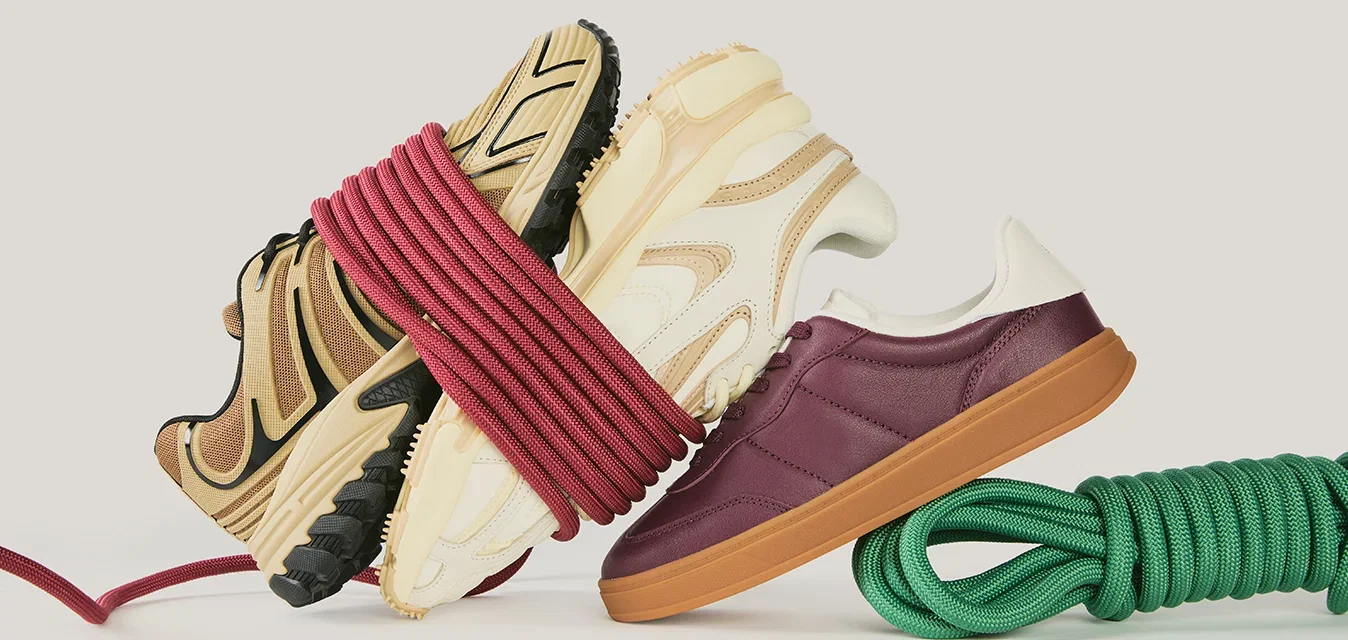 Drie sneakers opgestapeld en vastgebonden met een rood touw, naast een opgerold groen touw op een effen lichte achtergrond.