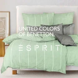 Grünes gestreiftes Bettwäsche-Set auf einem Bett mit verschiedenen grauen Kissen. Helle Holzmöbel und ein weich strukturierter Pouf in einem minimalistischen Zimmer.