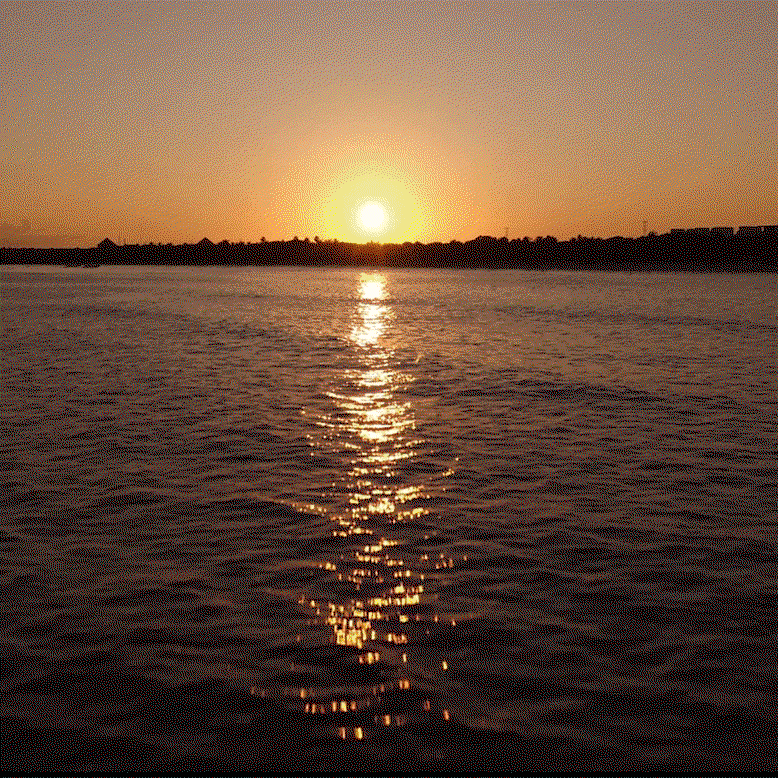 A glowing sunset shines across the shimmering surface of an ocean.