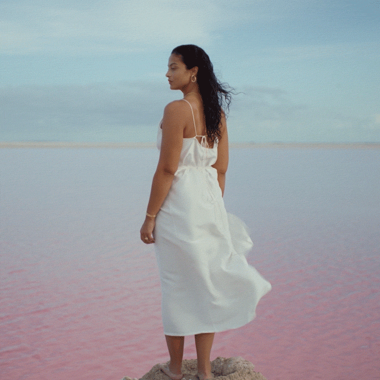 A model stands on a rock with their dress billowing in the wind.