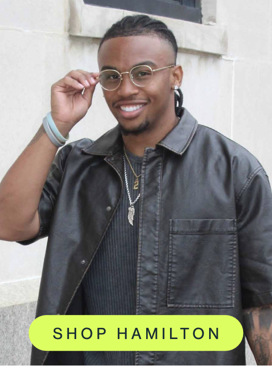 A smiling person wearing round gold blue light glasses and a black leather jacket adjusts their frames while standing outdoors. A bright "Shop Hamilton" button highlights the featured frame style.