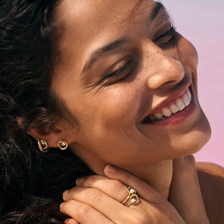 A model smiles as she wears 14k gold-plated pearl studs and rings.