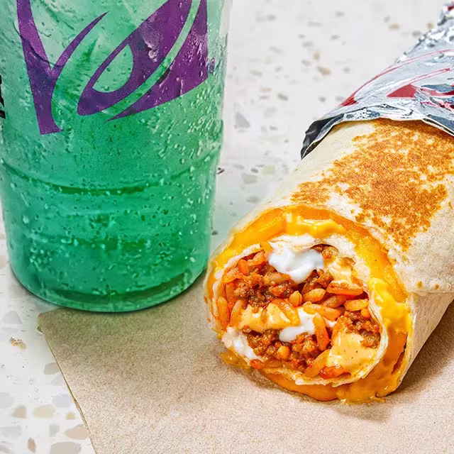 A close-up of a Taco Bell Quesarito next to a fountain drink on a counter.