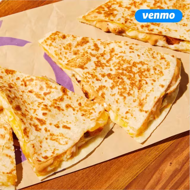Slices of a Taco Bell Chicken Quesadilla on its wrapper on a wooden table. Featuring a Venmo logo in the top right.
