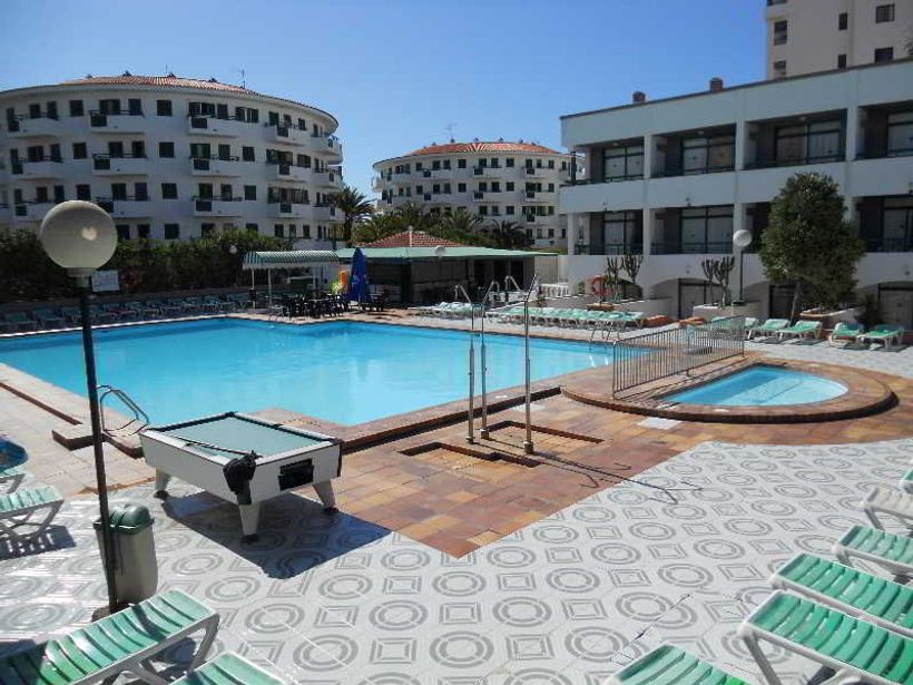 Hotel outdoor swimming pool with sun loungers, small round wading pool, pool table and white curved apartment buildings under blue sky