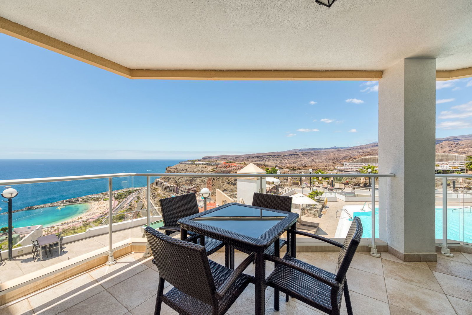 Balcony terrace with wicker table and four chairs overlooking the Atlantic sea, sandy beach, cliffs and resort pool