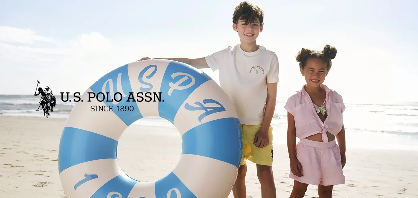 Zwei Kinder stehen barfuß an einem Sandstrand, eines hält einen großen blau-weißen aufblasbaren Schwimmring mit dem Text 