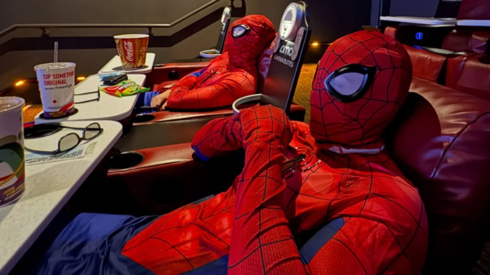 Two people in Spider-Man costumes recline in a movie theater