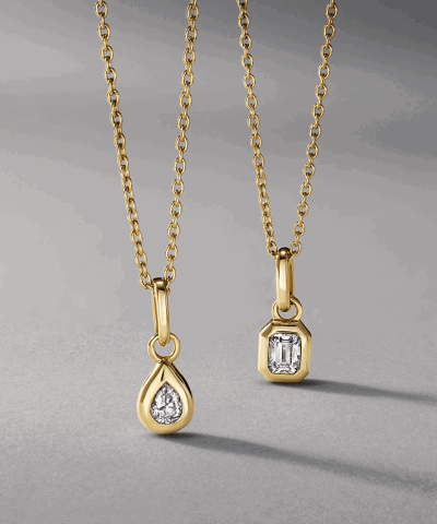 Two yellow gold necklaces featuring bezel-set pear-shaped and emerald-cut diamond pendants.