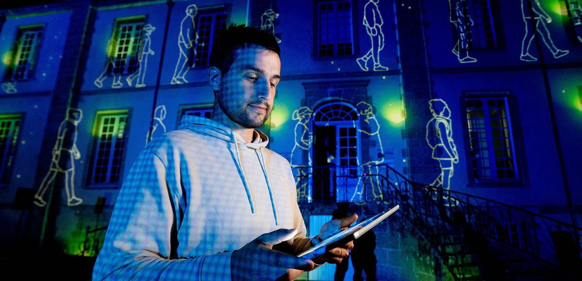 Philippe Dubost uses a tablet to fine-tune projected artwork on a historic building as part of an immersive exhibition installation.