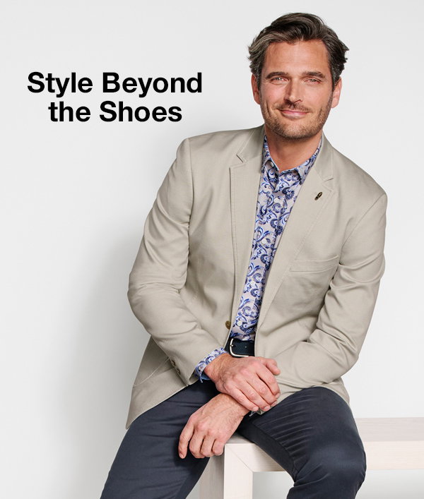 Model wearing a light neutral blazer over a blue patterned shirt with dark pants. Text reads: 