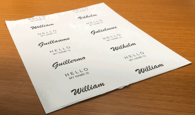 A sheet of name tags on a wooden surface, each with variations of the name William and the phrase “HELLO MY NAME IS.”.