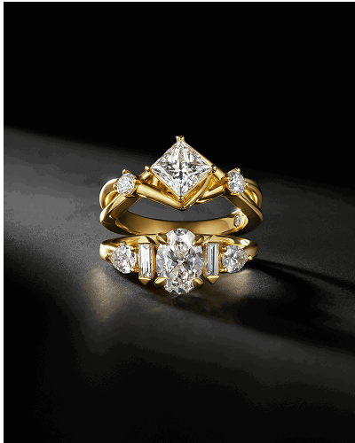 Two yellow gold diamond engagement rings on a dark background.