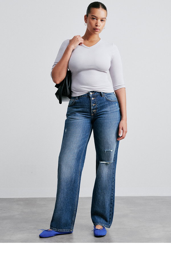 Model wearing white long sleeve top with distressed blue jeans and blue slippers